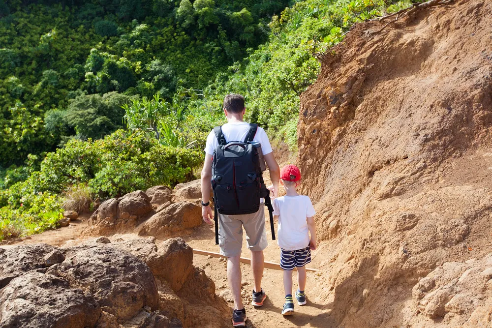 Hikers on a Kauai trail with lush green mountains and misty clouds